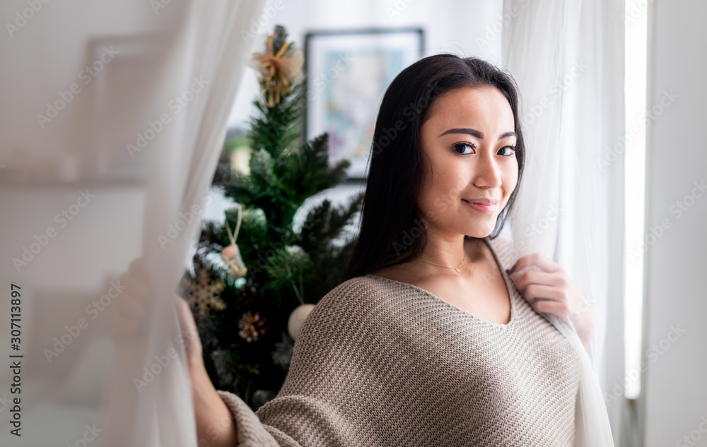 Happy asian woman standing near window in christmas decorated home Happy asian woman standing near window in christmas decorated home