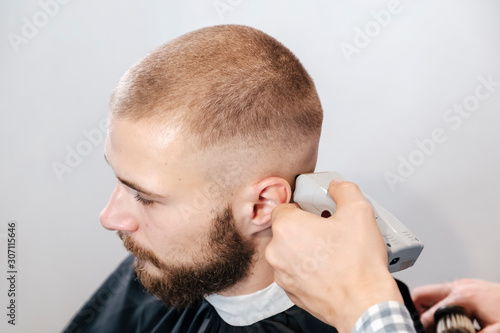 Barber shaves the bearded client's head with electric trimmer