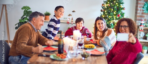 Beautiful family smiling happy and confident. Eating roasted turkey make selfie by smartphone celebrating christmas at home