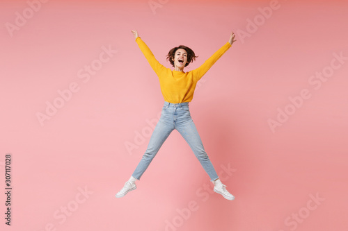 Funny young brunette woman girl in yellow sweater posing isolated on pastel pink background. People lifestyle concept. Mock up copy space. Having fun fooling around, spreading hands and legs, jumping.