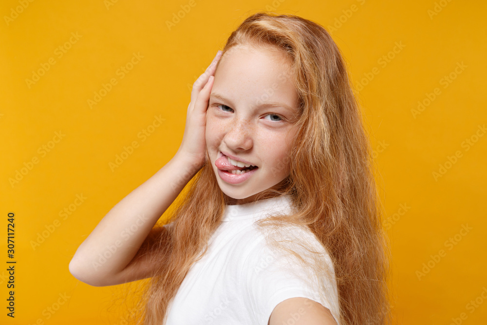 Fototapeta premium Close up of funny little ginger kid girl 12-13 years old in white t-shirt isolated on yellow background in studio. Childhood lifestyle concept. Mock up copy space. Doing selfie shot on mobile phone.