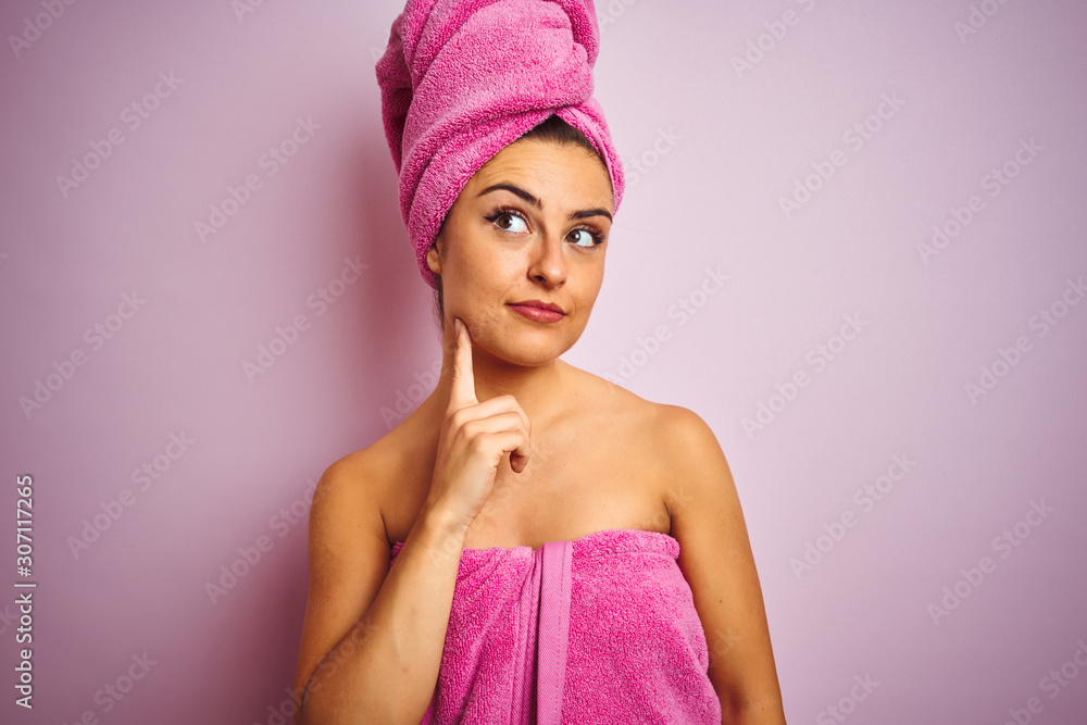 Young beautiful woman wearing towel after shower over isolated pink background with hand on chin thinking about question, pensive expression. Smiling with thoughtful face. Doubt concept. Young beautiful woman wearing towel after shower over isolated pink background with hand on chin thinking about question, pensive expression. Smiling with thoughtful face. Doubt concept.