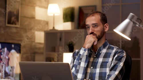 Businessman thinking and holding arms crossed while working on laptop