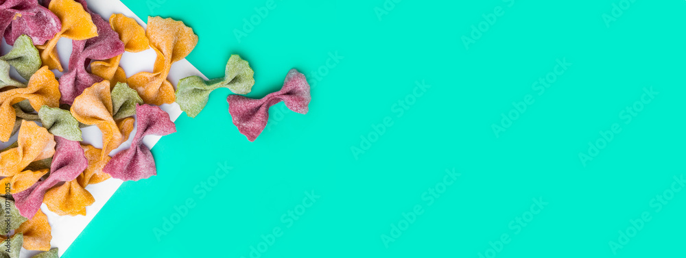 Pile of Italian dried Tri Color Farfalle pasta. Various colors of bow tie on trendy green mint color background