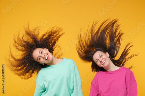 Foto Two cheerful women friends european african american girls in pink green clothes posing isolated on yellow background