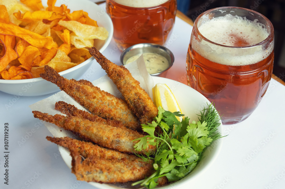 Mug with beer and beer snacks. Fried fish with chips and sauce.