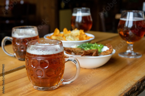 Mug with beer and beer snacks. Corn chips with sauce, fish and greens.
