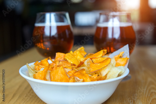 A plate with potato chips on the background of glasses with beer in a bar on the table.
