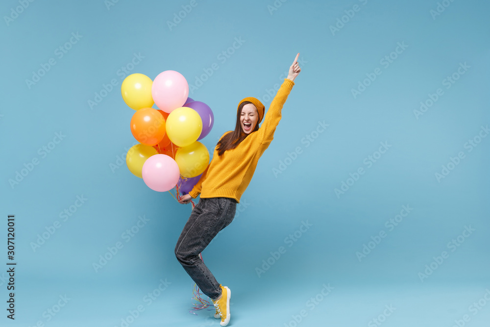 Young woman girl in sweater and hat posing isolated on blue background. Birthday holiday party people emotions concept. Mock up copy space. Celebrating hold colorful air balloons dance rising hand up. Young woman girl in sweater and hat posing isolated on blue background. Birthday holiday party people emotions concept. Mock up copy space. Celebrating hold colorful air balloons dance rising hand up.