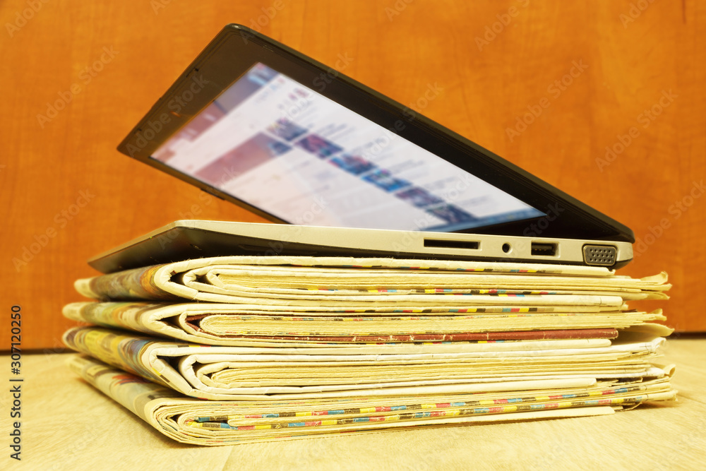 Stack of Newspapers and Laptop. Personal Computer and Business Magazines. Concept for News - Different Sources of Information Stack of Newspapers and Laptop. Personal Computer and Business Magazines. Concept for News - Different Sources of Information