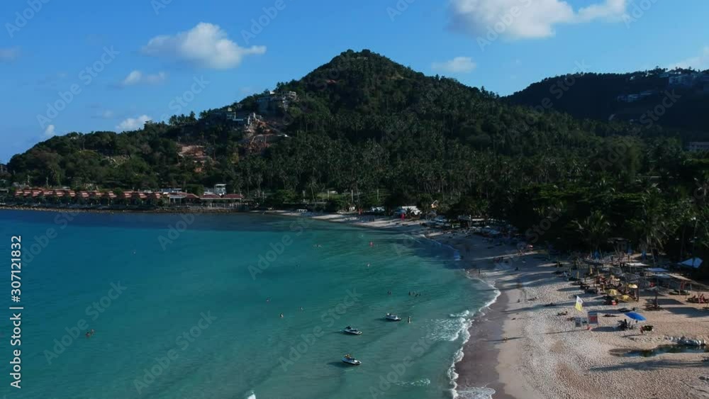 Aerial Elevating Drone Shot. Flying near the ocean coast. View of the sea waves, sandy beach, green hill, blue water and palm trees. The island Samui, Thailand. Aerial Elevating Drone Shot. Flying near the ocean coast. View of the sea waves, sandy beach, green hill, blue water and palm trees. The island Samui, Thailand.