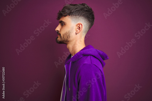 Fototapeta Naklejka Na Ścianę i Meble -  Young man with tattoo wearing striped polo standing over isolated yellow background looking to side, relax profile pose with natural face with confident smile.