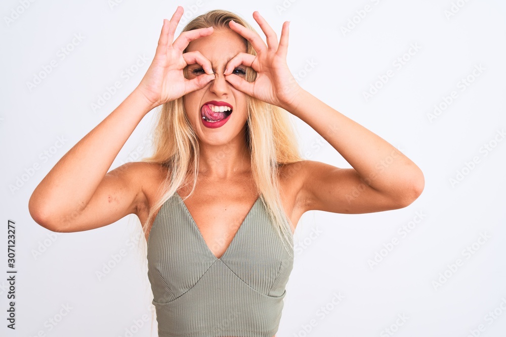Fototapeta premium Young beautiful woman wearing casual green t-shirt standing over isolated white background doing ok gesture like binoculars sticking tongue out, eyes looking through fingers. Crazy expression.