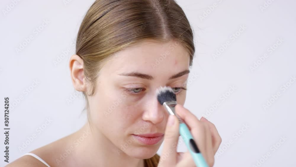 Close up shot with grey background. Young beautiful woman applying primer with brush while doing her makeup Close up shot with grey background. Young beautiful woman applying primer with brush while doing her makeup