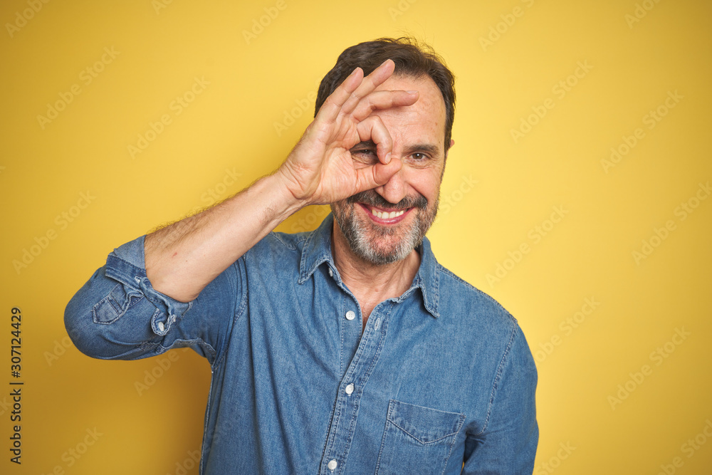 Handsome middle age senior man with grey hair over isolated yellow background doing ok gesture with hand smiling, eye looking through fingers with happy face. Handsome middle age senior man with grey hair over isolated yellow background doing ok gesture with hand smiling, eye looking through fingers with happy face.