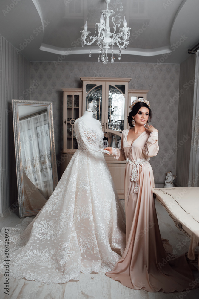 Romantic atmosphere of the bride's morning. Beautiful bride in wedding dress. Bride in a home. Bride morning preparation. Bride in beautiful dress near the mannequin with dress indoors at home.