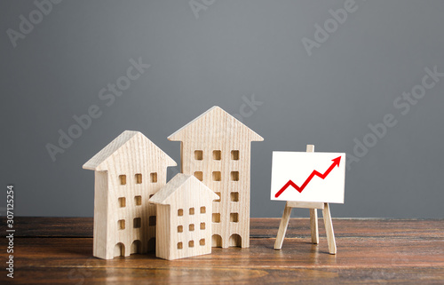 Residential buildings and easel with a positive growth trend red arrow up chart. Market growth, attracting investment. Raising taxes and house maintenance. Real estate price increases. High value photo