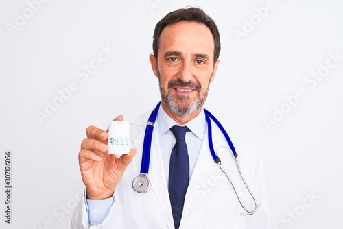 Middle age doctor man holding pills standing over isolated white background with a confident expression on smart face thinking serious