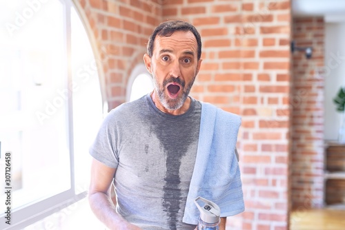 Schilderij op canvas Middle age handsome sportman sweaty holding bottle of water and towel after exer