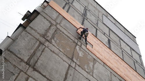 Insulation of walls of house. Worker hanging on the ropes installs heat shield
