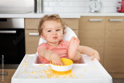 Funny toddler eating pasta in high chair with foot on table