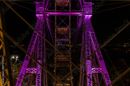 Two empty cars behind several steel wires on a giant ferris wheel covered in purple light