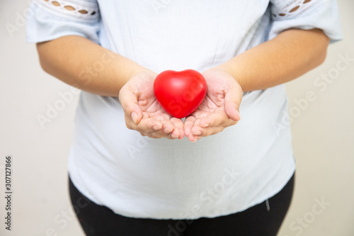 Pregnant women holding red hearts, Concept: Family expectations Happy lifestyle,mother in dress holds hands on belly,