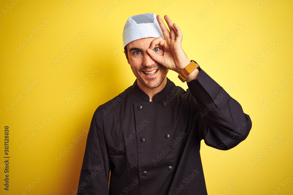 Young handsome chef man cooking wearing uniform and hat over isolated yellow background doing ok gesture with hand smiling, eye looking through fingers with happy face. Young handsome chef man cooking wearing uniform and hat over isolated yellow background doing ok gesture with hand smiling, eye looking through fingers with happy face.