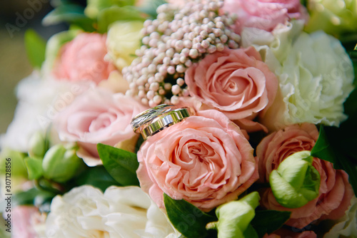 Close up of two golden wedding rings on bridal bouquet of pink and white roses outdoors  copy space. Selective focuse. Wedding concept