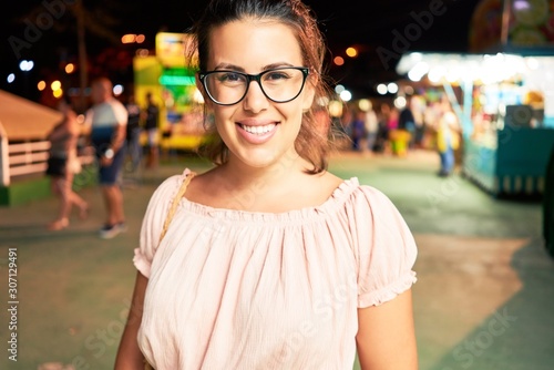 Young beautiful woman wearing glasses smiling happy and excited at funfair around lights at night © Krakenimages.com