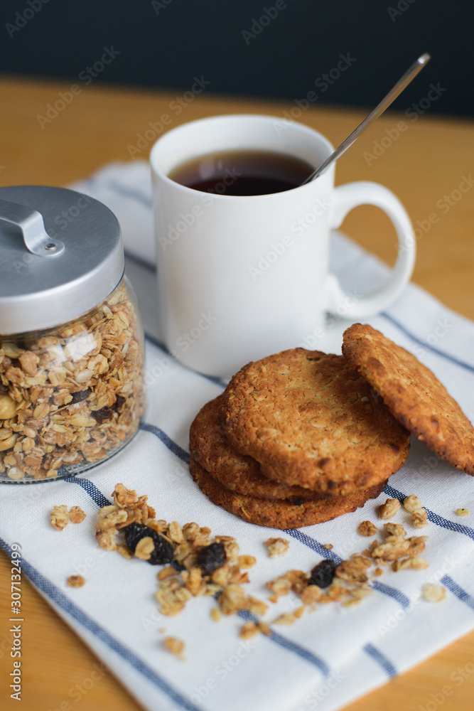 round brown wholemeal oatmeal cookies stack with granola and black coffee in white cup on striped textile napkin on wooden table, close up side view of vertical still life stock photo image round brown wholemeal oatmeal cookies stack with granola and black coffee in white cup on striped textile napkin on wooden table, close up side view of vertical still life stock photo image