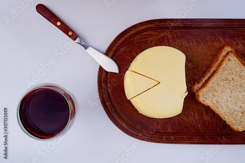 Top view of glass of red wine, cheese and bread on wooden cutting board.