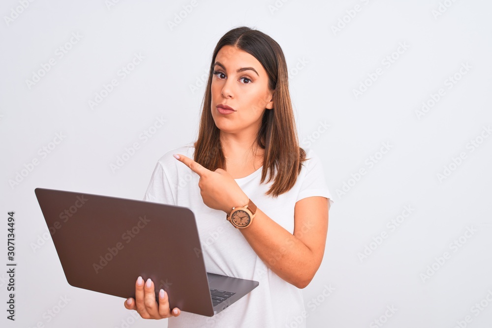 Beautiful young woman working using computer laptop over white background Pointing with hand finger to the side showing advertisement, serious and calm face Beautiful young woman working using computer laptop over white background Pointing with hand finger to the side showing advertisement, serious and calm face