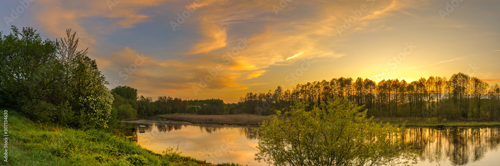 evening spring landscape. panoramic view of the river with a hilly grassy shore against a cloudy sky with a glow from sunset