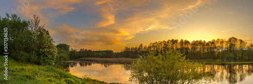 evening spring landscape. panoramic view of the river with a hilly grassy shore against a cloudy sky with a glow from sunset