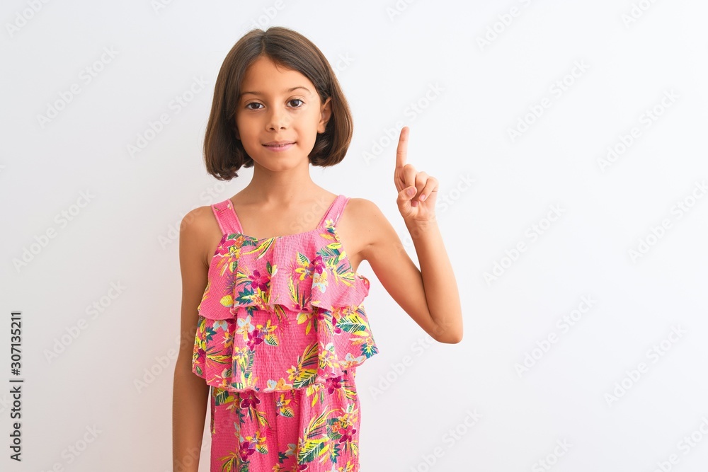 Young beautiful child girl wearing pink floral dress standing over isolated white background showing and pointing up with finger number one while smiling confident and happy. Young beautiful child girl wearing pink floral dress standing over isolated white background showing and pointing up with finger number one while smiling confident and happy.