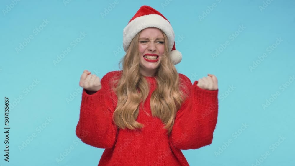 Displeased pretty woman in christmas hat becoming angry and screaming over turquoise background Displeased pretty woman in christmas hat becoming angry and screaming over turquoise background