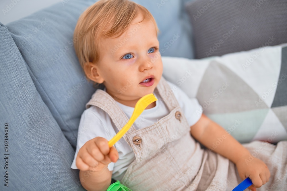 Adorable blonde toddler sitting on the sofa playing with plastic meals toys at kindergarten Adorable blonde toddler sitting on the sofa playing with plastic meals toys at kindergarten