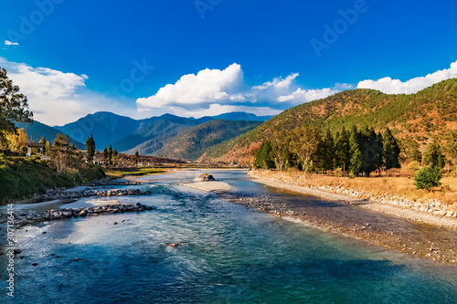 Mo Chhu River on a nice sunny day, Punakha, Bhutan. View from the wooden cantilever bridge near Punakha Dzong to river, houses of Punakha city and Himalaya mountains covered with forest. © sunday_morning