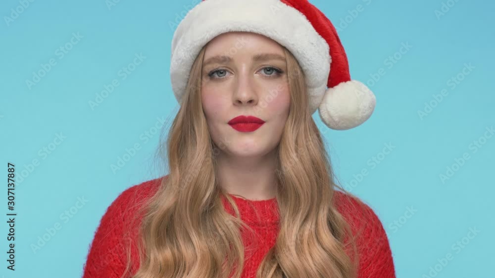 Close up view of Cheerful mystery pretty woman in christmas hat winks with eye and looking at the camera over turquoise background Close up view of Cheerful mystery pretty woman in christmas hat winks with eye and looking at the camera over turquoise background