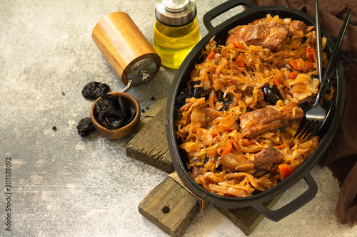 Polish or Czech dish. Sauerkraut stewed with bacon, prunes and meat ribs in a cast-iron frying pan on a stone or slate countertop. Copy space.