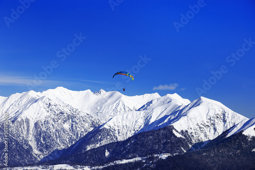 Panoramic view of winter peaks of mountains covered snow. Natural landscapes for travel and sport. Flying paraglider above Caucasus mountain.