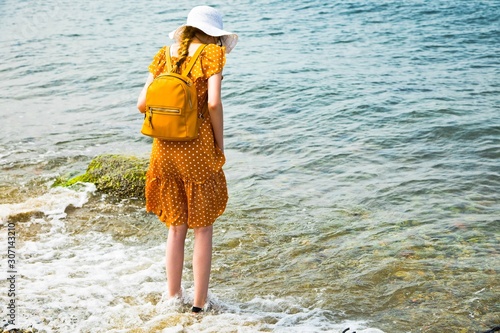 A girl in yellow summer dress staying on beach