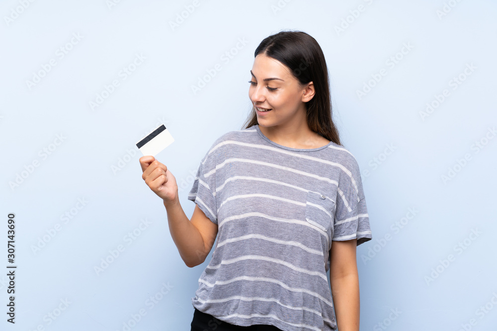 Young brunette woman over isolated blue background holding a credit card Young brunette woman over isolated blue background holding a credit card