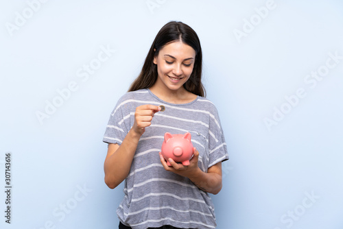 Young brunette woman over isolated blue background holding a big piggybank