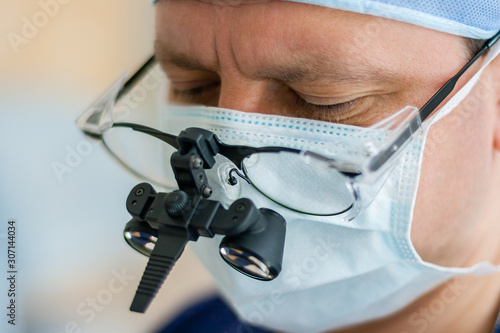 Male surgeon in magnifying glasses with binocular loupes is in a hospital.