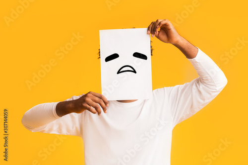 Obraz na płótnie Black man putting paper with sad emoji over his face
