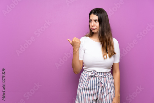Young woman over isolated purple background unhappy and pointing to the side © luismolinero