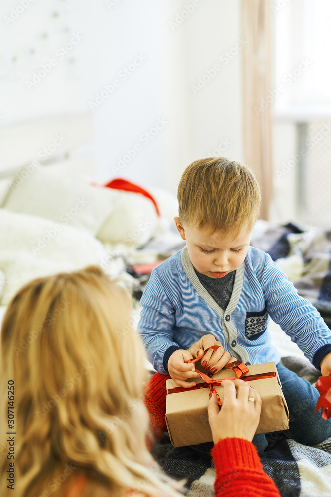 Young woman presenting Christmas gift to her little son at Chrismas morning in bed. Celebrating Christmas and New Year, having fun, happy time together. Young woman presenting Christmas gift to her little son at Chrismas morning in bed. Celebrating Christmas and New Year, having fun, happy time together.