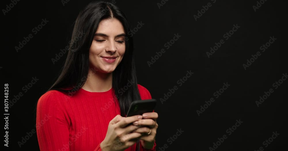 Girl writes sms girlfriend. Brunette writes sms and laughs .Girl using smartphone and typing isolated over black background. Girl writes sms girlfriend. Brunette writes sms and laughs .Girl using smartphone and typing isolated over black background.